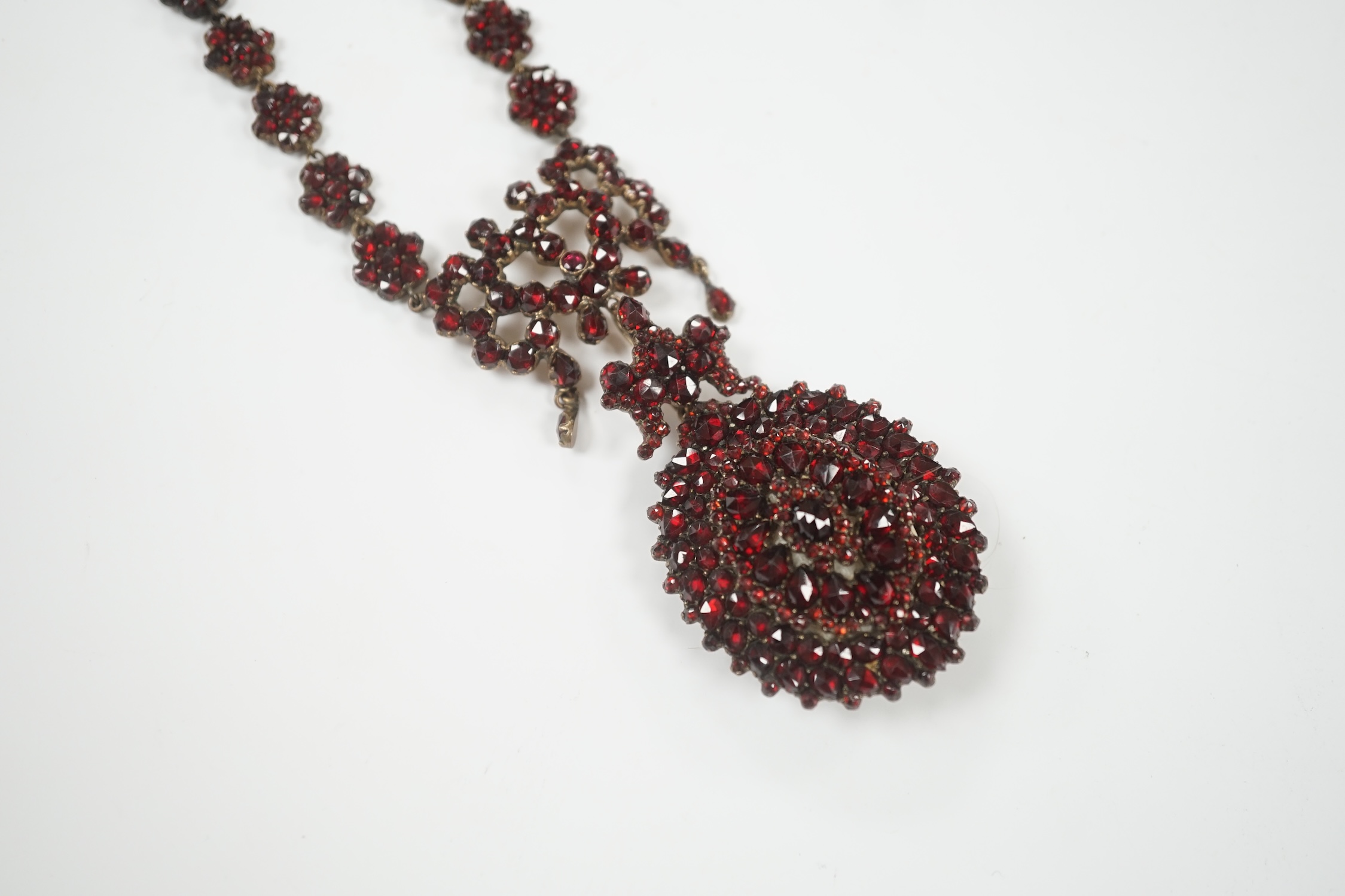 A Victorian gilt metal and facet cut garnet cluster set mourning drop pendant necklace, overall 50cm.